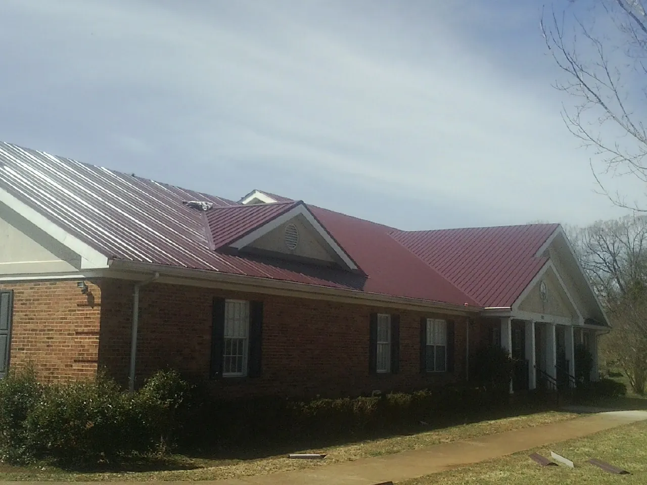 Red metal roof with gabled entries on a long brick building, from a Hail Damage Roof Repair job in Queensbury