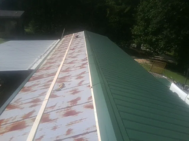 Old rusted panels beside newly installed green metal roofing — Wind Damage Roof Repair by Roofing Brothers in Queensbury