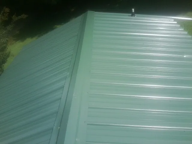 New green metal panels meeting at the ridge of a roof — Flat Roof Repair work by our crew in Queensbury