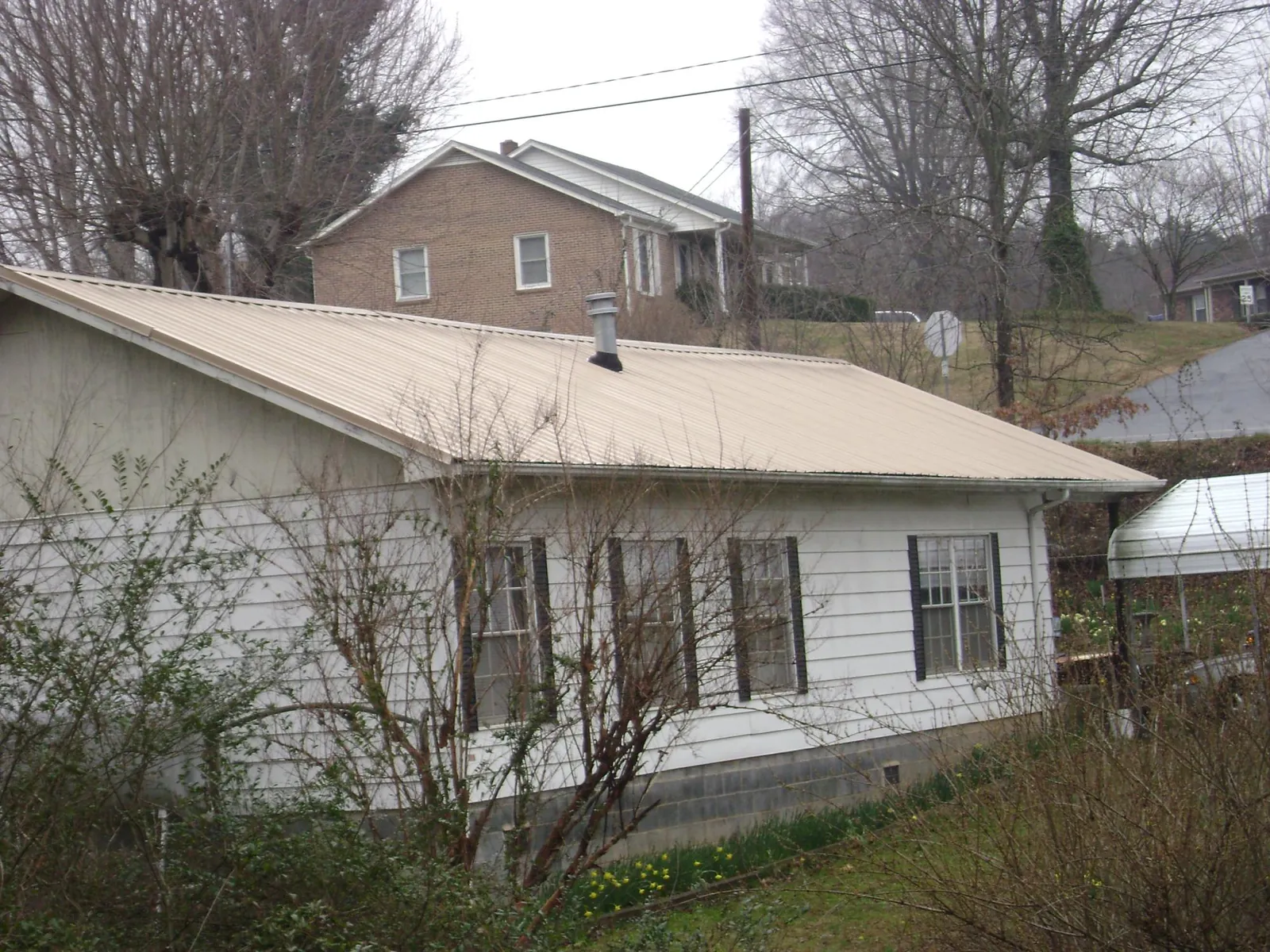 Tan metal roof on a white sided house set into a hillside — Commercial Roofing by Roofing Brothers in Queensbury