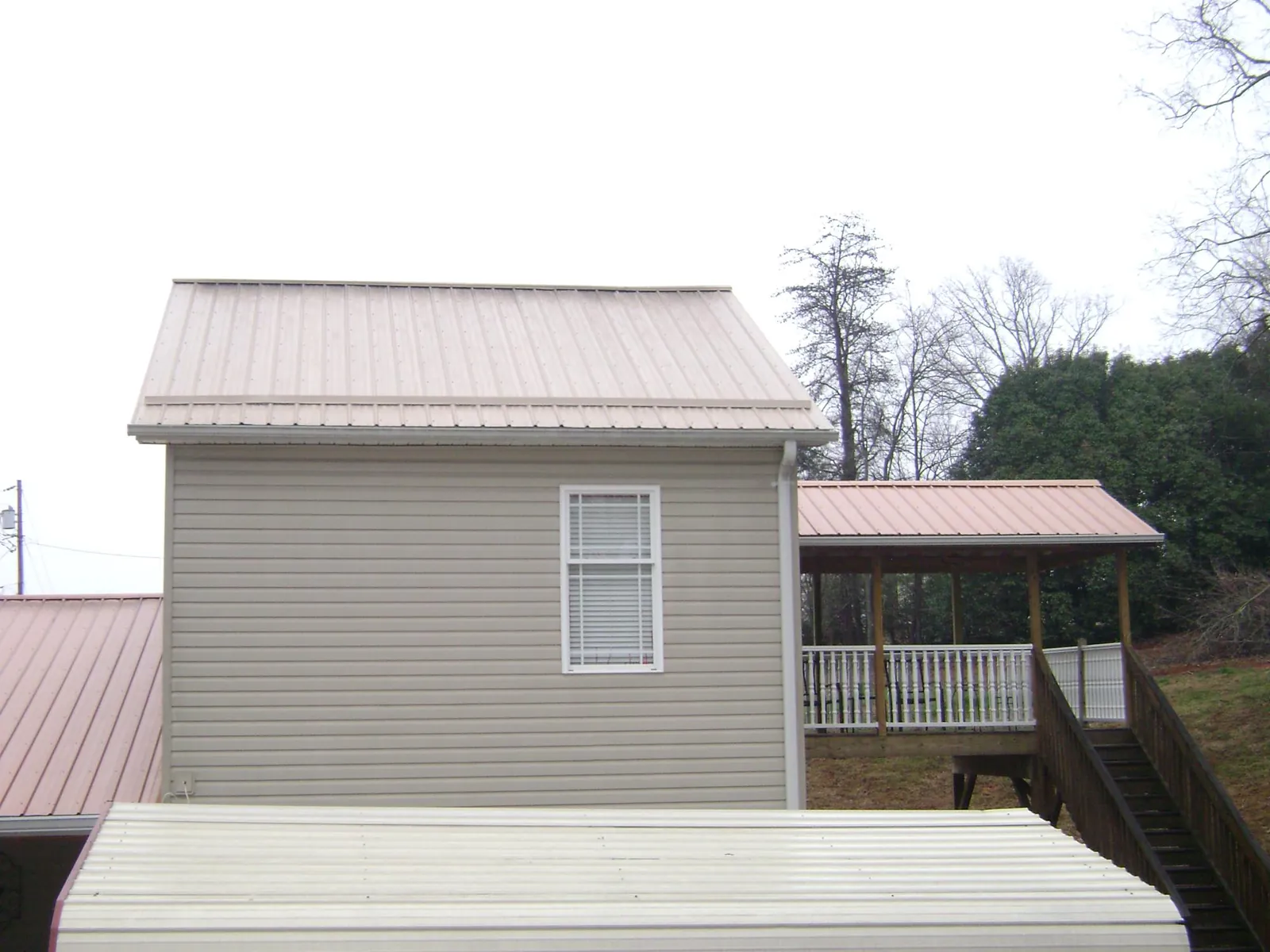 Tan metal roofs on a two story addition and attached porch, from a Roof Replacement job in Queensbury
