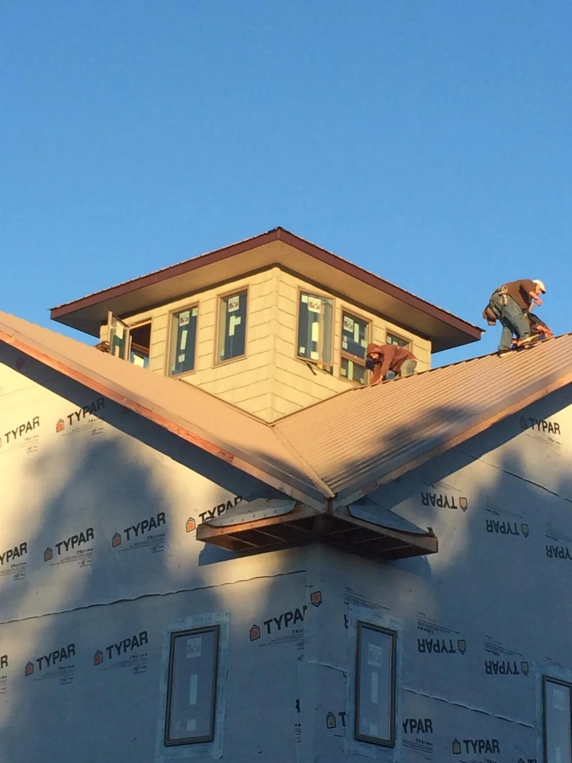 Roofers working around a rooftop cupola on a new metal roof at sunset — Roof Waterproofing in Queensbury by Roofing Brothers